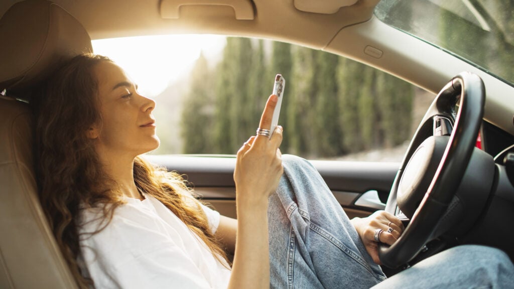 Ung kvinna som kollar på sin mobiltelefon samtidigt som hon kör utan säkerhetsbälte.