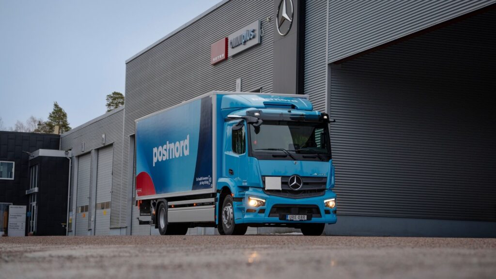 En blå eldriven lastbil från PostNord, en Mercedes-Benz eActros, parkerad framför Veho Bil i Västerås. Symbol för PostNords satsning på hållbara leveranser.