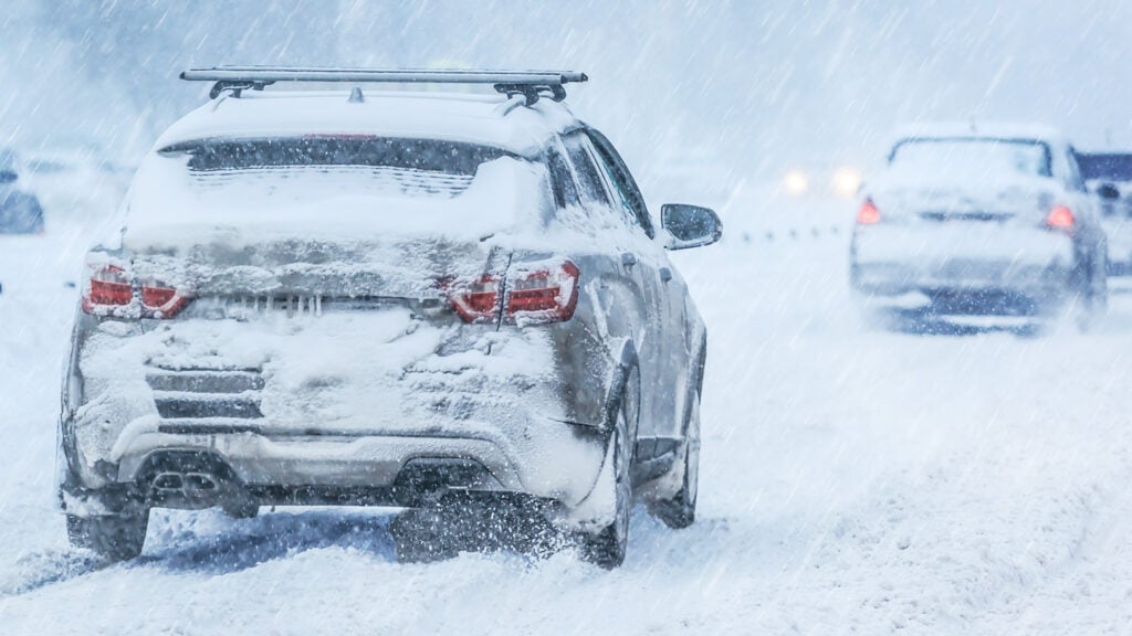 Översnöad bil utan tända bakljus i vinterväder.
