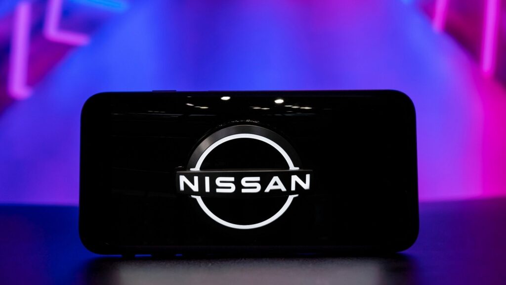 Närbild av Nissans logotyp visad på en mobilskärm, med en futuristisk bakgrund i blått och lila.