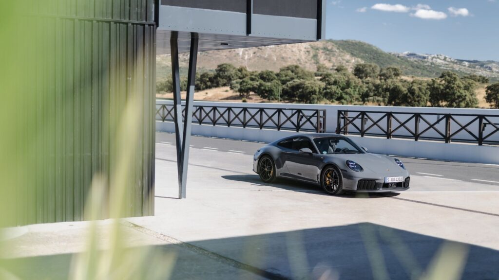 En grå Porsche 911 parkerad vid en modern byggnad med bergslandskap i bakgrunden, vilket speglar bilens popularitet i ett exklusivt land med låg fordonsskatt.