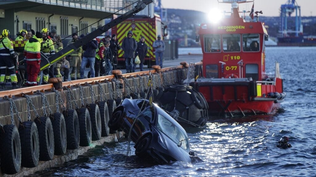 En Tesla lyfts upp ur Oslofjorden av räddningstjänsten, omgiven av brandmän och en räddningsbåt. Bilen är delvis nedsänkt i vattnet.