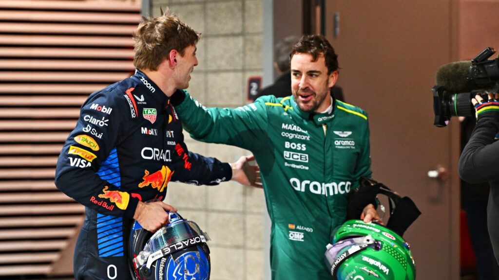 Max Verstappen i Red Bull-ställ och Fernando Alonso i Aston Martin-kläder står tillsammans och ler medan de håller sina hjälmar.
