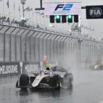 F2-bilar kör genom ösregnet på Albert Park Circuit i Melbourne, med kraftiga vattenstrålar bakom sig. Skyltarna för FIA och Formel 2 syns tydligt ovanför banan medan förarna försöker navigera i de svåra förhållandena.