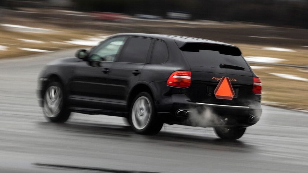 A-traktor ombyggd från svart Porsche Cayenne med varningstriangel bak, fotograferad i rörelse på landsväg.