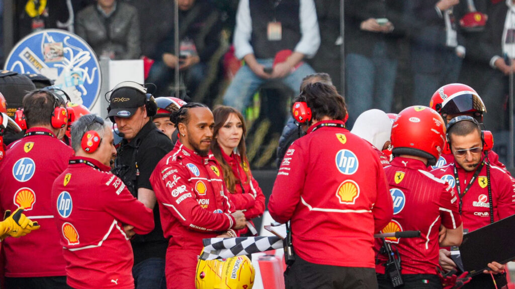 Lewis Hamilton iklädd Ferrari-overall står med sitt team under ett event.
