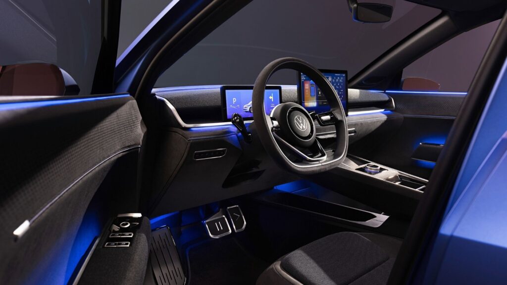 Interiör av Volkswagen ID.2 med en modern förarmiljö, dubbla skärmar och fysiska knappar för kritiska funktioner som volym och klimatkontroll.