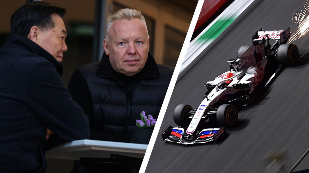 Dmitry Mazepin sitter vid ett bord utanför en hospitality-svit i F1-depån i Bahrain, klädd i svart väst och omgiven av två personer i samtal.