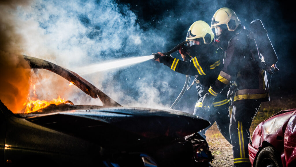 Två brandmän släcker en bilbrand.
