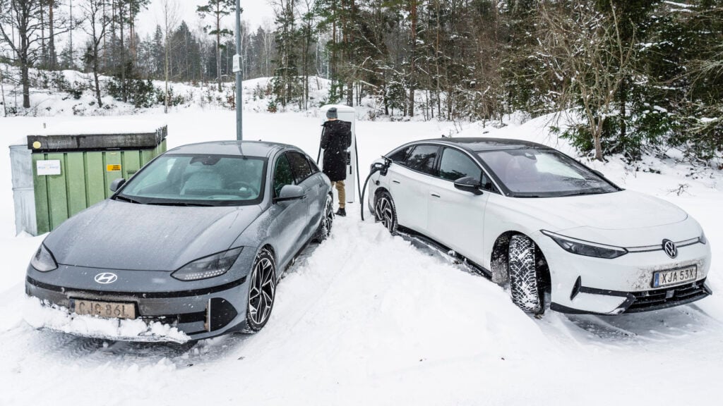 Två elbilar laddar på en parkering full av snö.