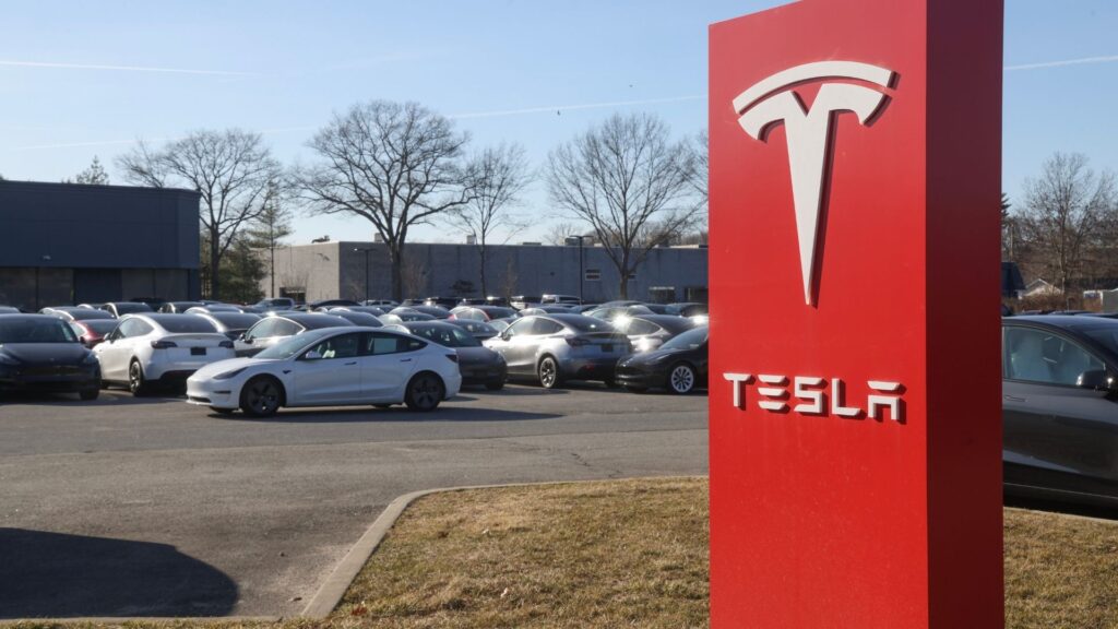 Tesla Model 3 och Model Y står parkerade framför ett återförsäljningscenter med röd Tesla-skylt.