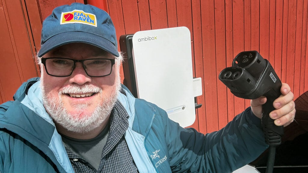 Reporter Magnus Fröderberg håller upp en DC-laddsladd med dubbelriktad laddning framför en laddbox från Ambibox.