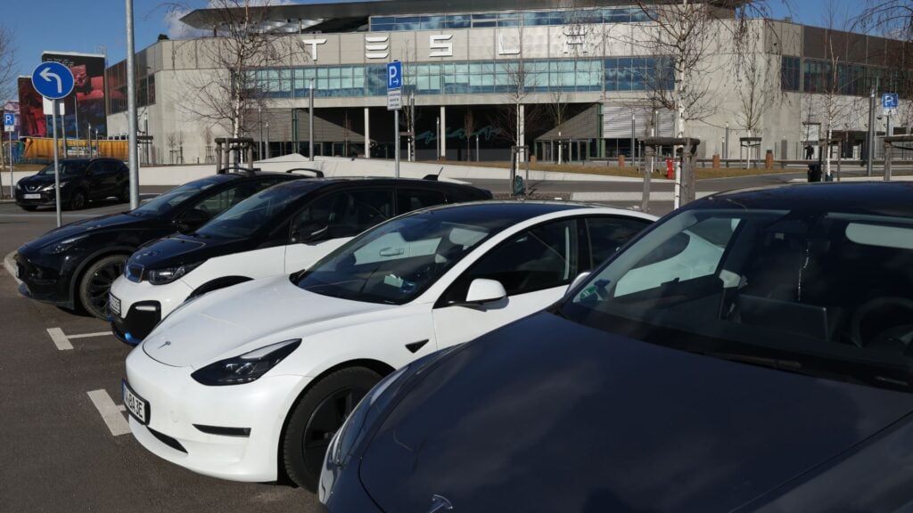 Flera Teslabilar parkerade utanför en Tesla-anläggning i dagsljus.