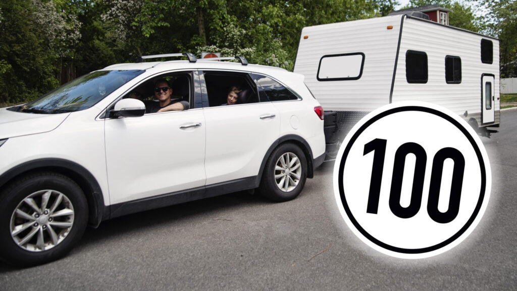 Vit bil med vit husvagn och en Tempo 100-skylt