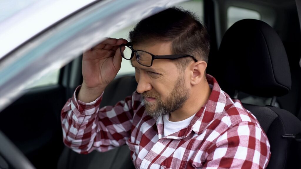 Förare i bil sätter på sig glasögon – illustration av synproblem i trafiken.