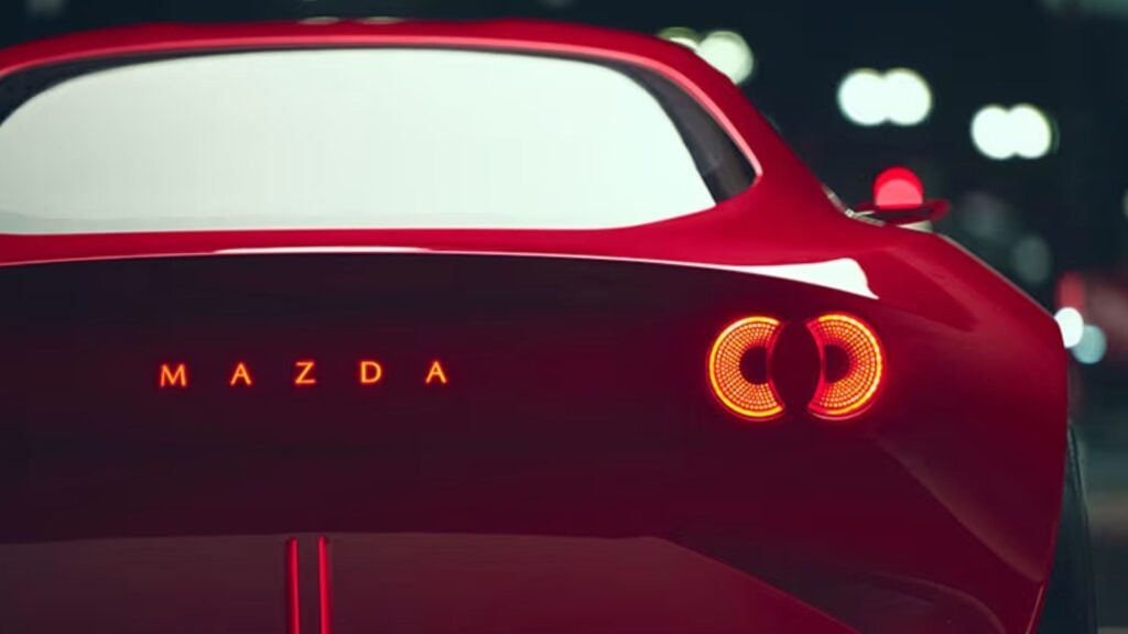 Nattbild på bakpartiet av Mazda Iconic SP i röd lack, med distinkta LED-baklyktor och upplyst Mazda-logotyp.