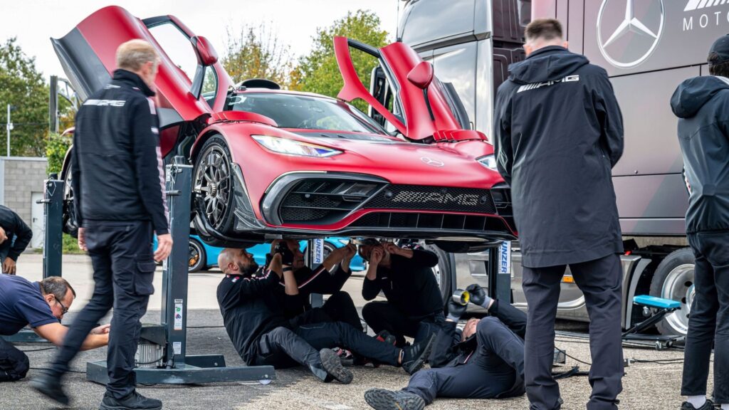 Mercedes-AMG One med uppfällda dörrar undersöks av flera mekaniker under service. Återkallas på grund av brandrisk i hydrauliken.