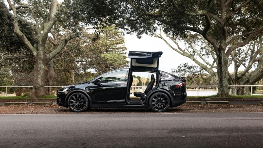 Svart Tesla Model X med öppna falkvingedörrar, parkerad vid väg i naturmiljö