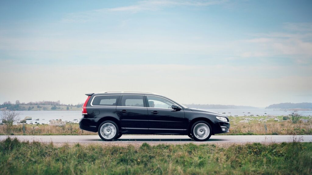 Svart Volvo V70 kombi kör på landsväg vid svensk kust.