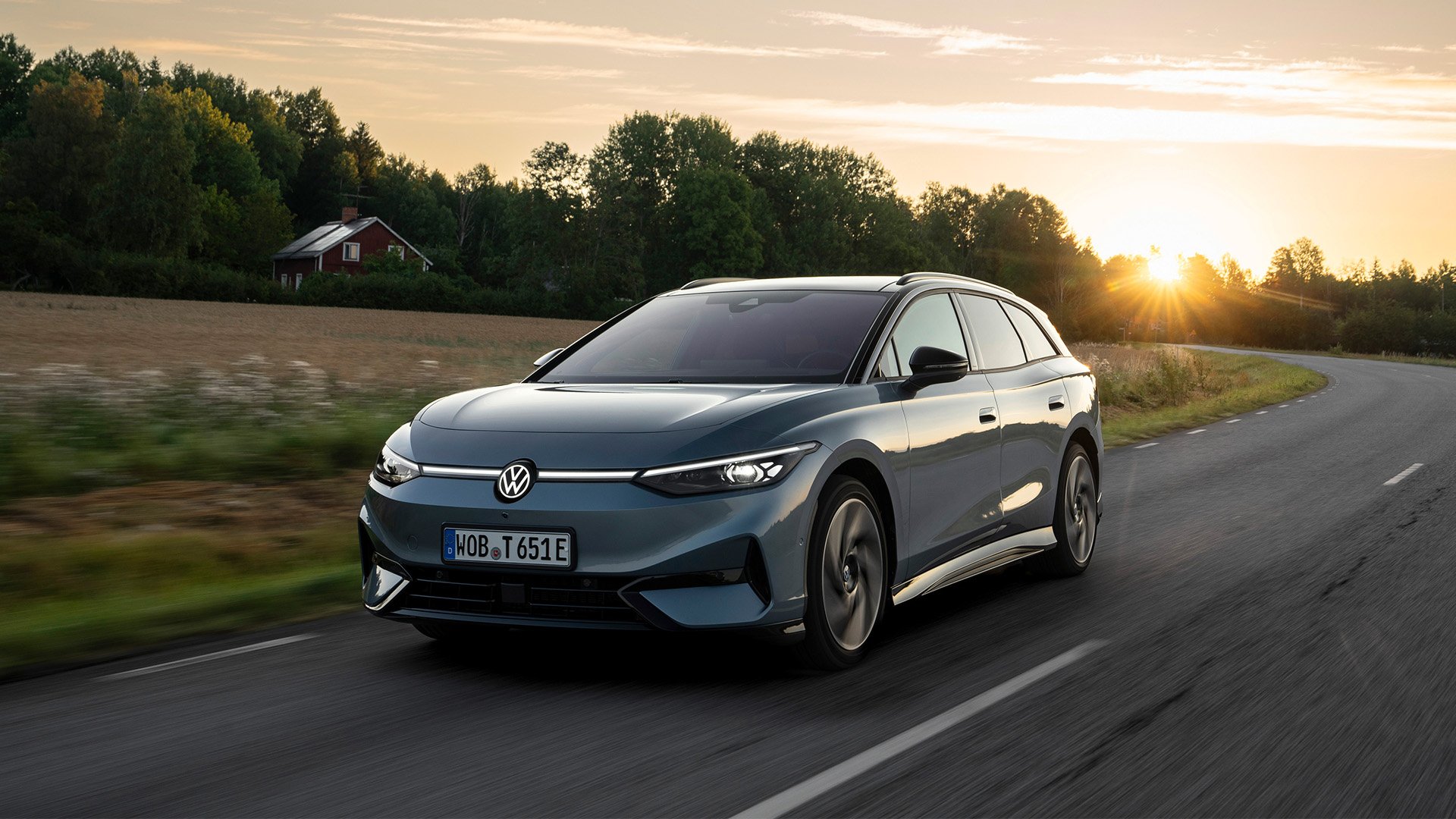 Grå Volkswagen ID.7 Tourer Pro S kör på landsväg med solnedgång i bakgrunden.