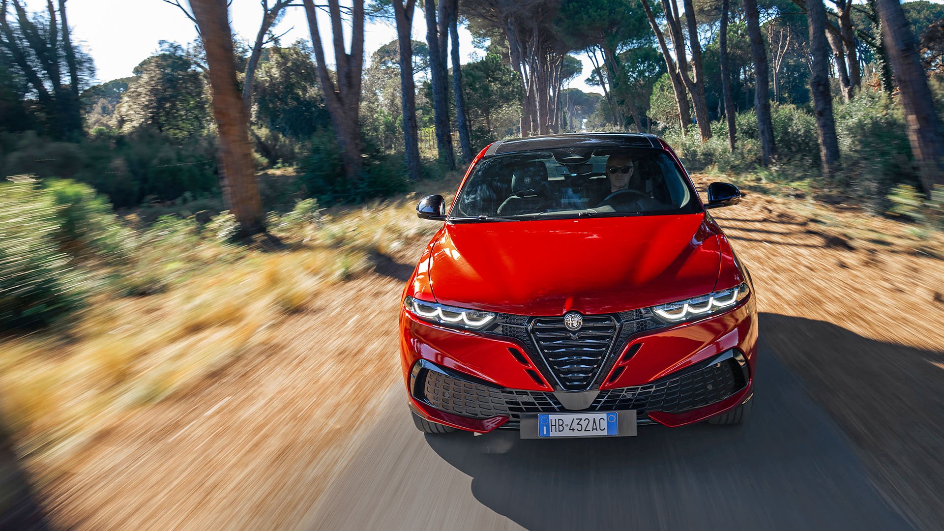 Röd Alfa Romeo Tonale på landsväg fotad framifrån.