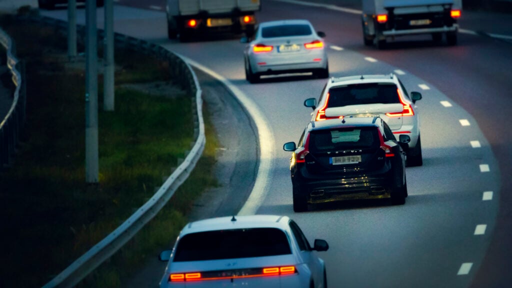 Bil kör på motorväg med i skymningen med släckta bakljus.