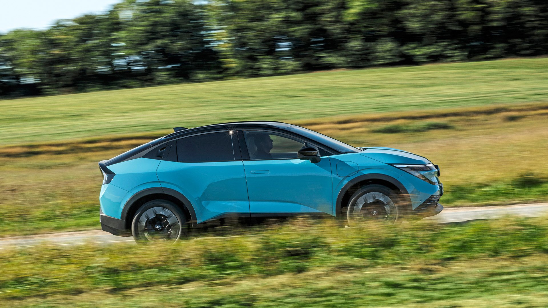 Ljusblå Nissan Leaf i profil kör på landsväg.