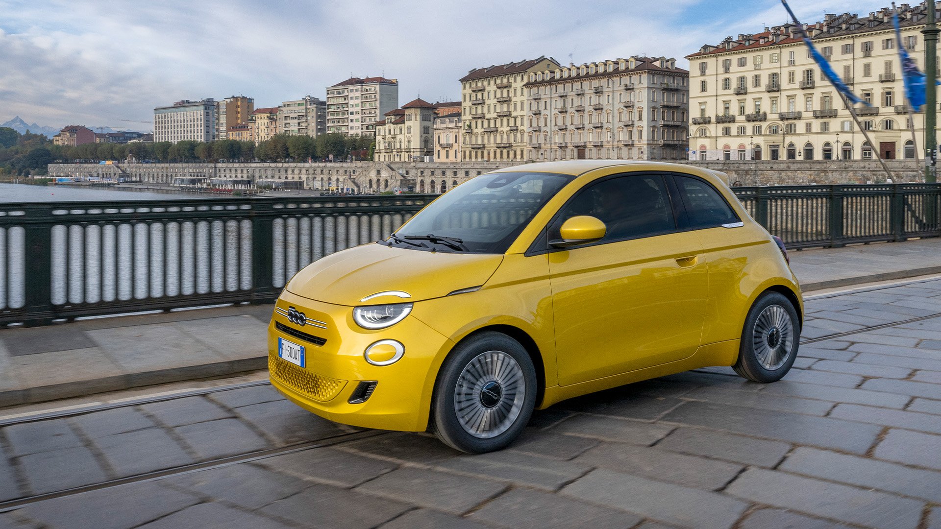 Gul Fiat 500 Hybrid Torino parkerad med stadsbakgrund.
