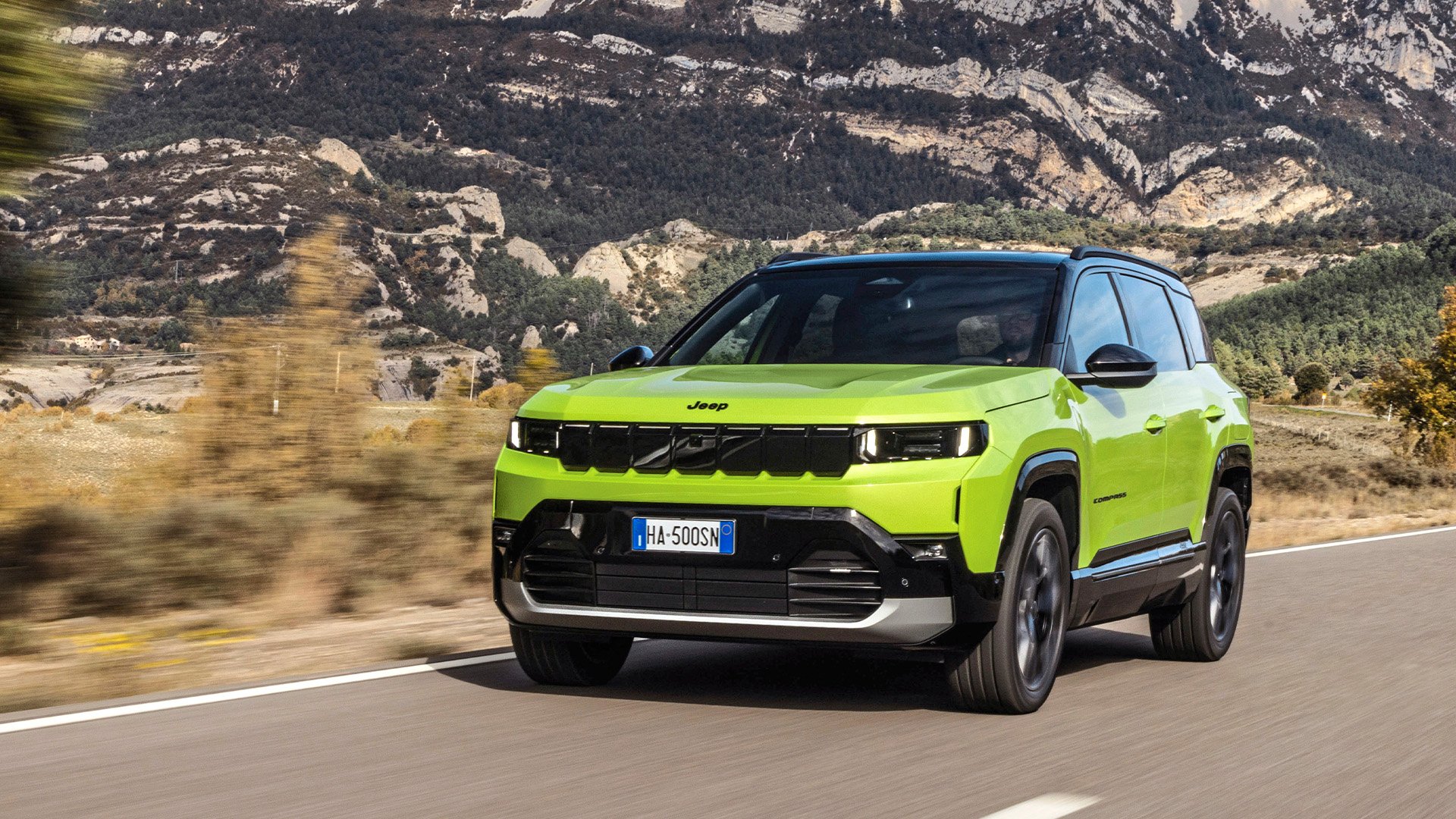 Neongrön Jeep Compass på väg med berg i bakgrunden.