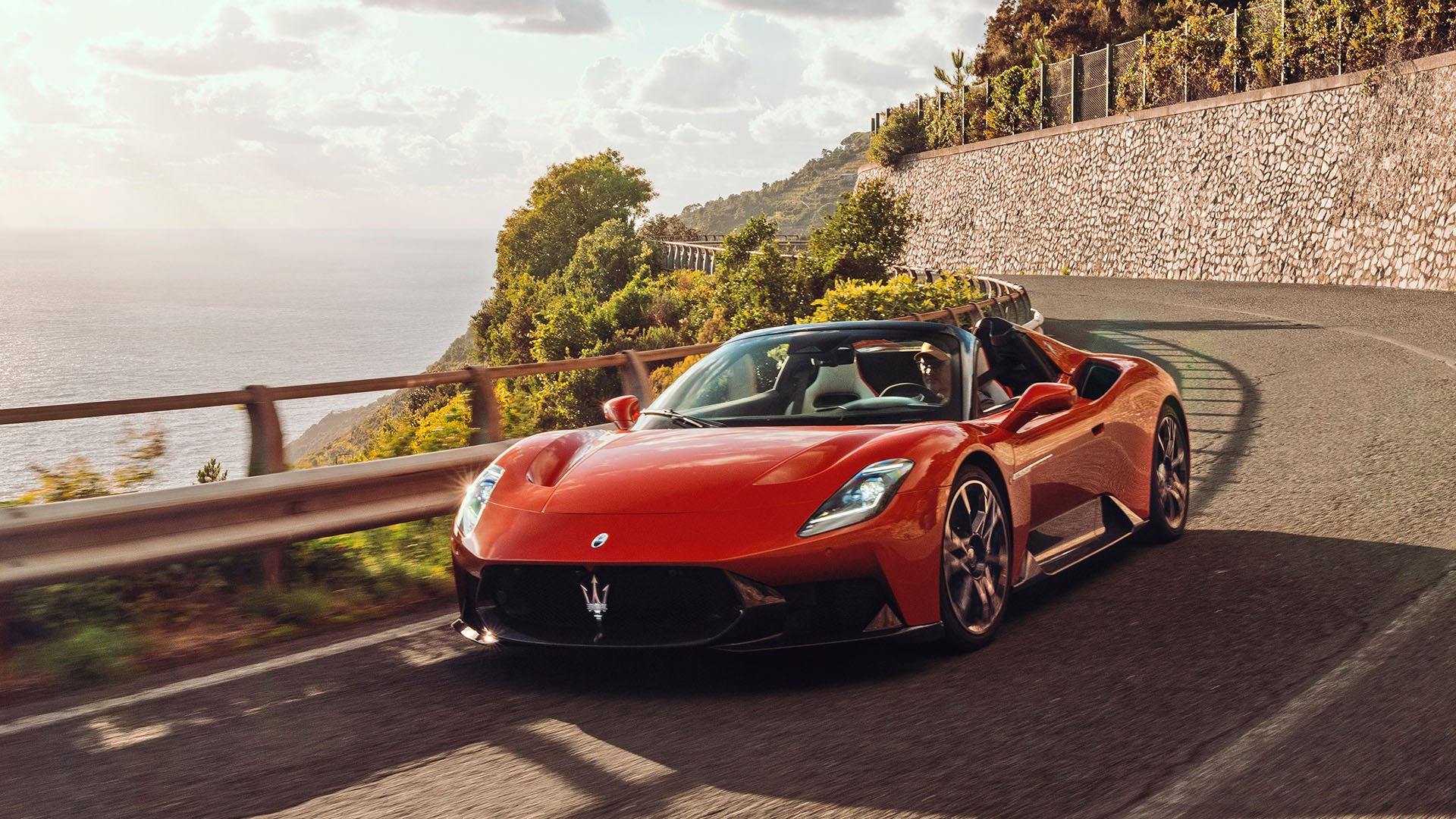 Röd Maserati MCPura kör längs landsväg med havet i bakgrunden.