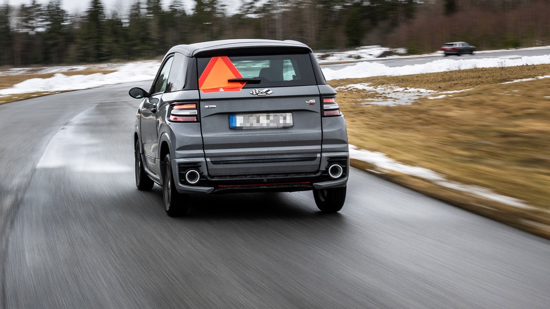 Mopedbil på blöt väg med snö på sidorna