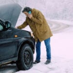 Man står på vinterväg med nedkyld bil och öppen motorhuv.