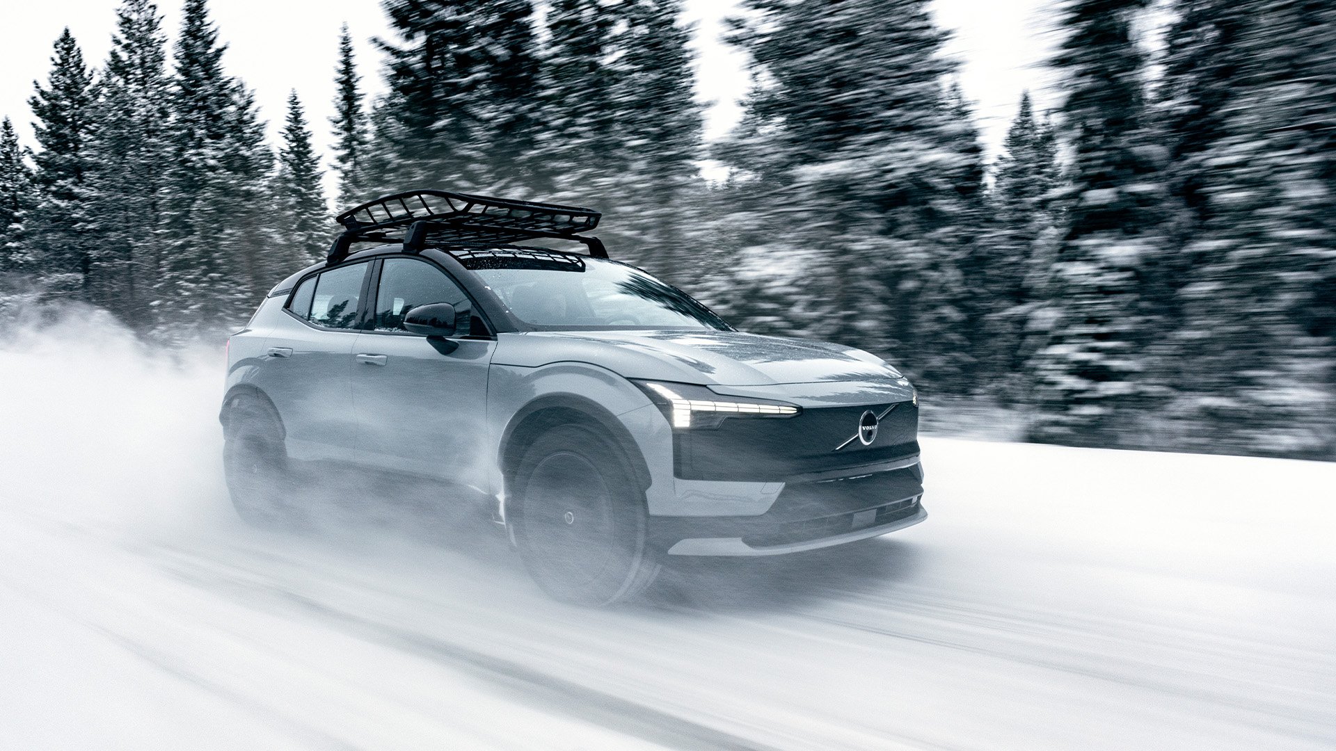 En grå Volvo EX30 Cross Country kör på snöig landsväg.