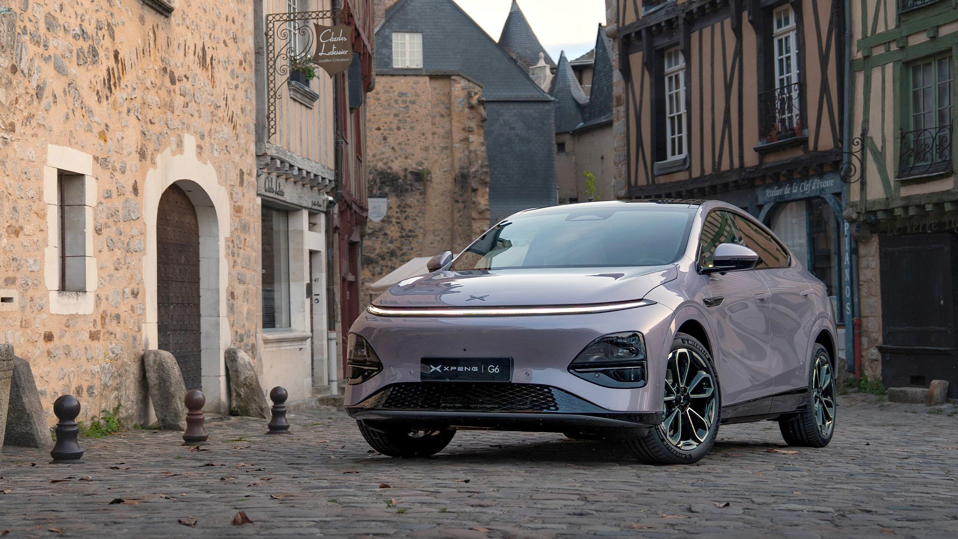 Lila Xpeng G6 parkerad på kullerstensväg med tegelhus bakom.
