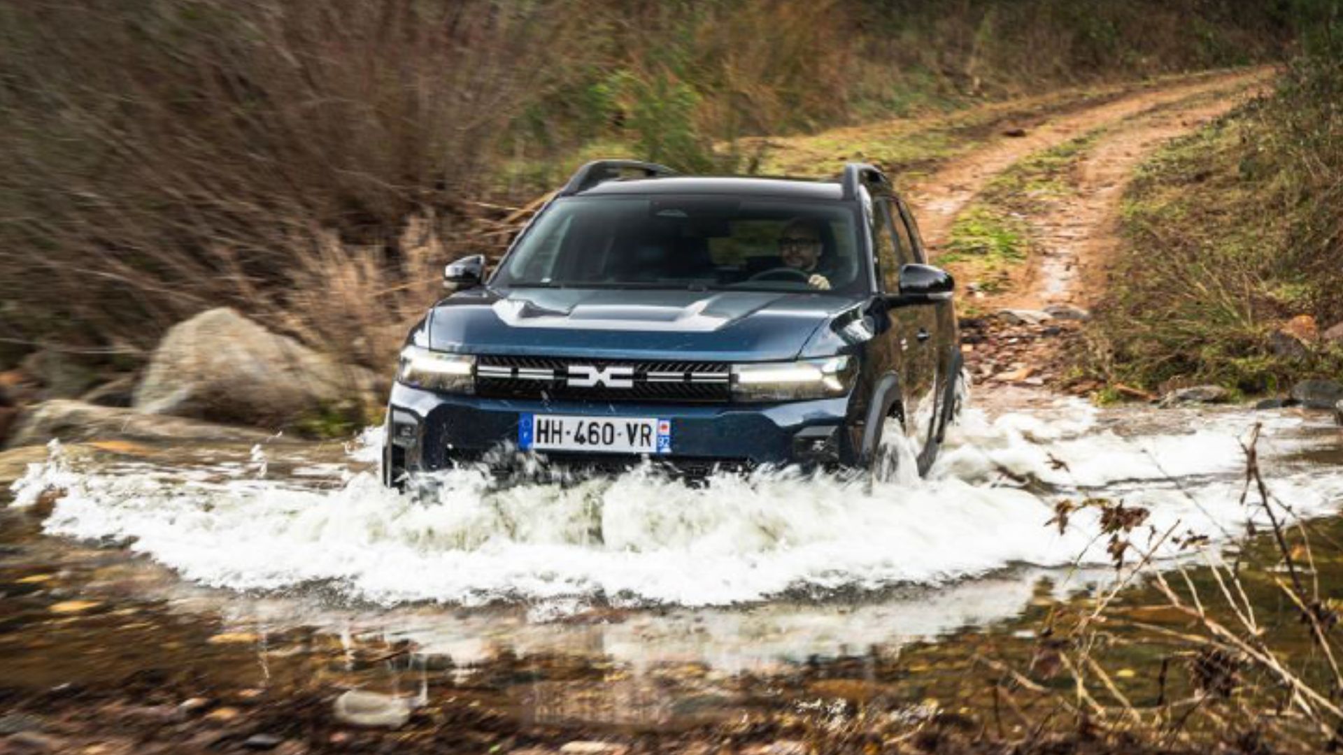 Blå Dacia Duster Hybrid-G 150 4x4 kör genom vatten i terräng