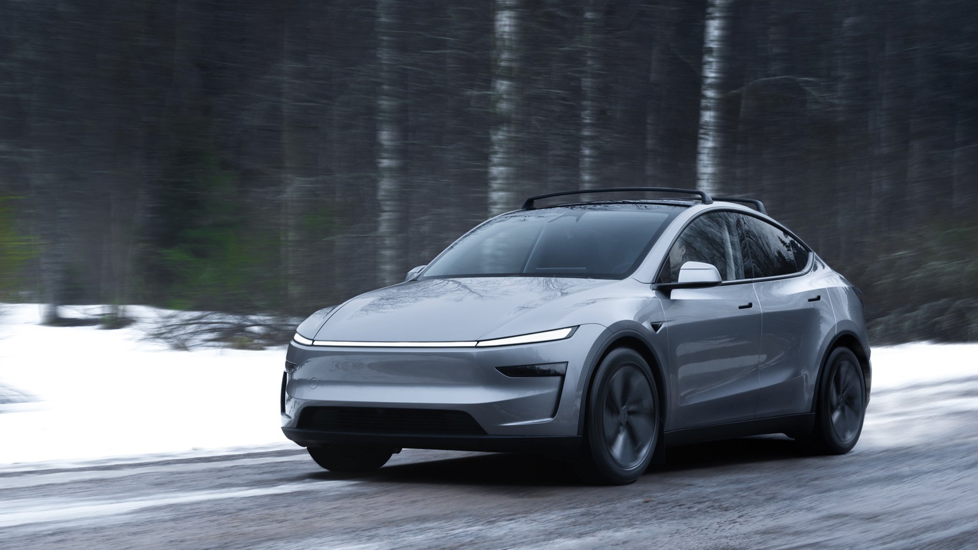 Grå Tesla Model Y kör på snöig landsväg.