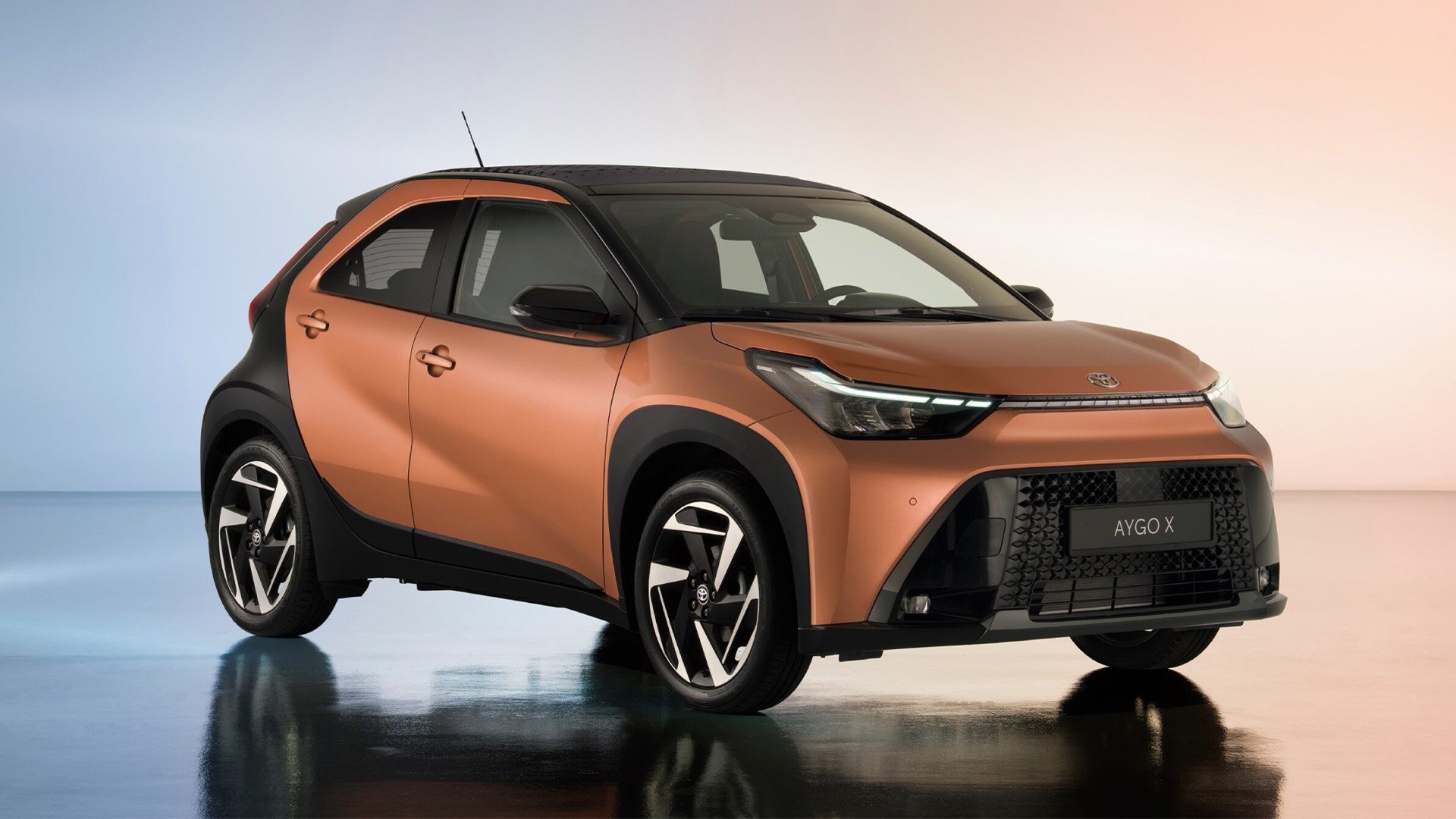 Bronsfärgad Toyota Aygo X snett framifrån i studio.