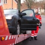 Bärgningsbil lastar en stillastående personbil på en villagata i Sverige