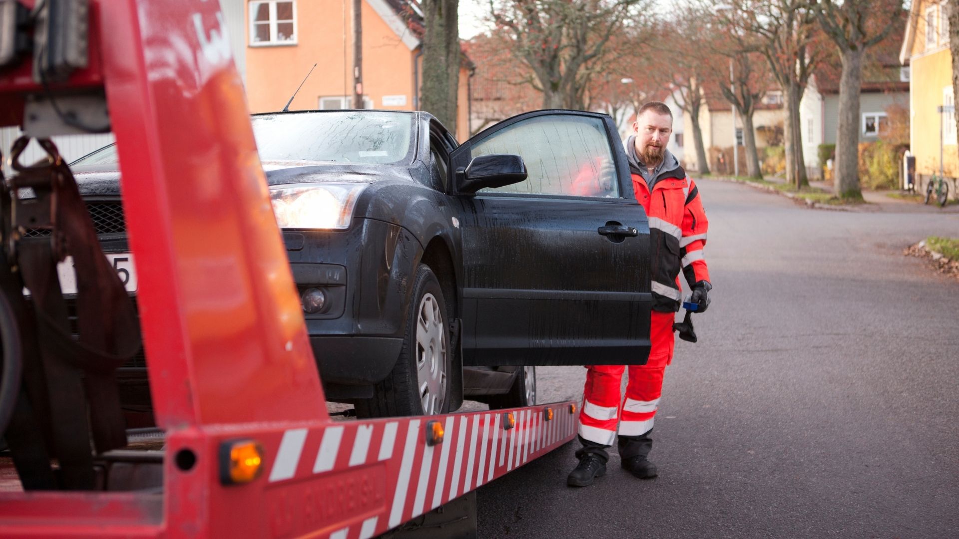 Bärgningsbil lastar en stillastående personbil på en villagata i Sverige