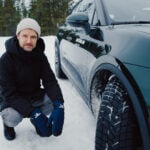 John Sempill på huk bredvid en mörkgrön Porsche Macan i snö.