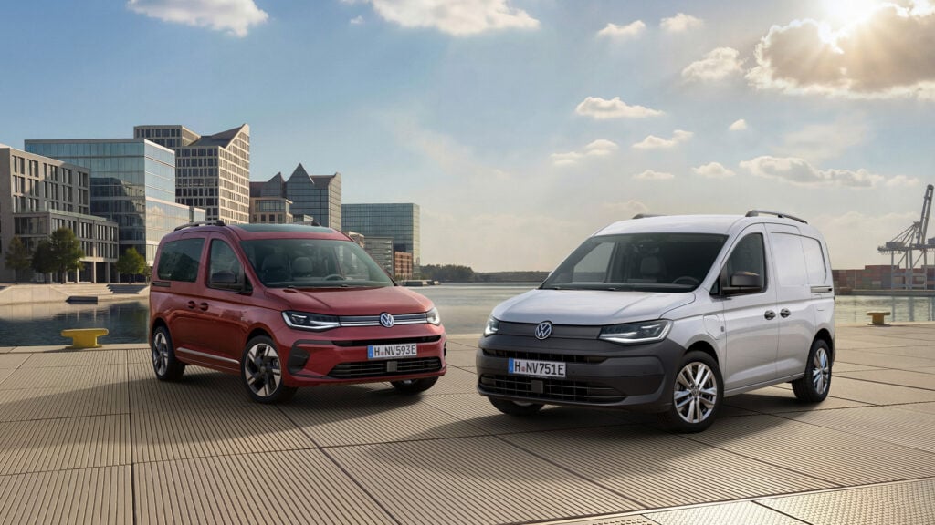 Vinröd Volkswagen Caddy och en vit Caddy modellår 2027 framför bostäder.