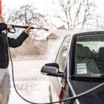 Man lite frånvänd från kameran tvättar sin bil med högtryck.