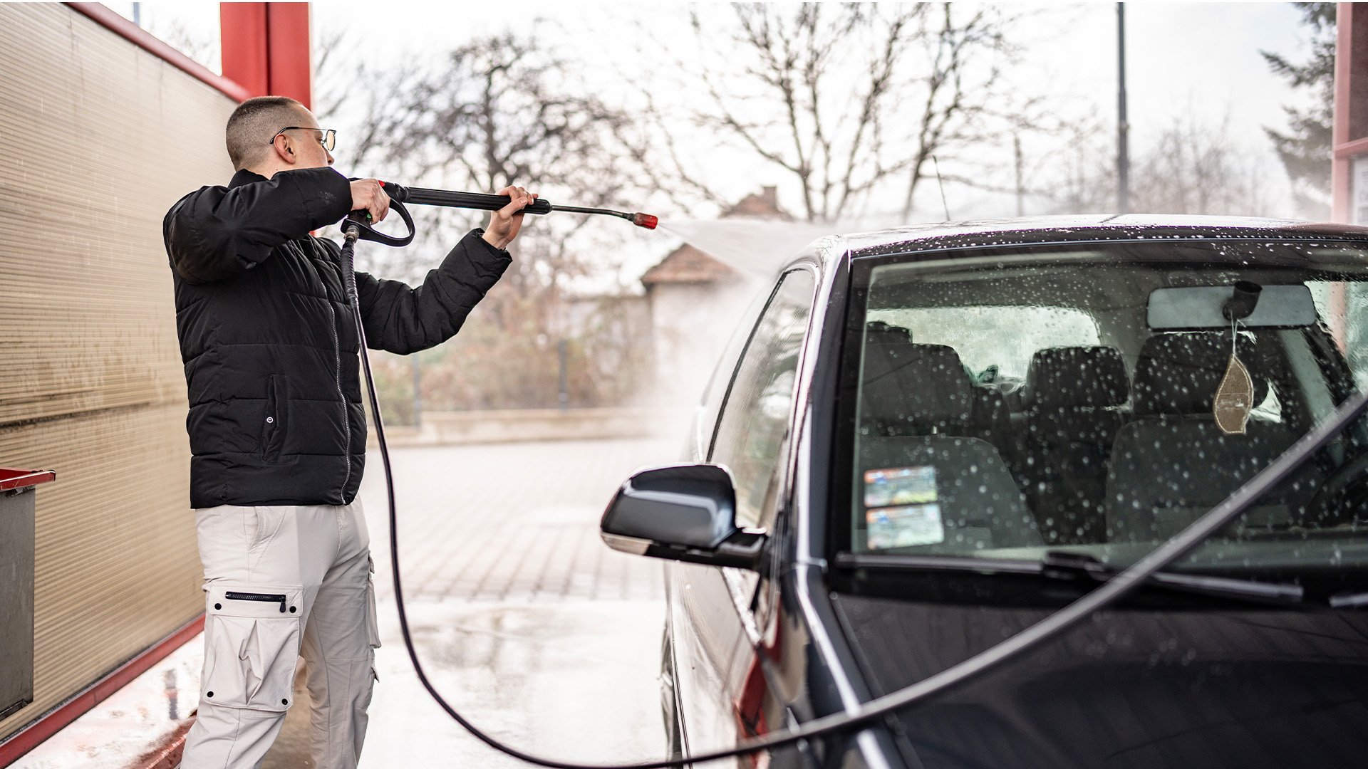 Man lite frånvänd från kameran tvättar sin bil med högtryck.