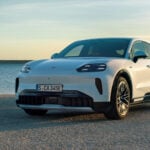Vit Porsche Cayenne Coupé Electric snett framifrån med havet bakom.