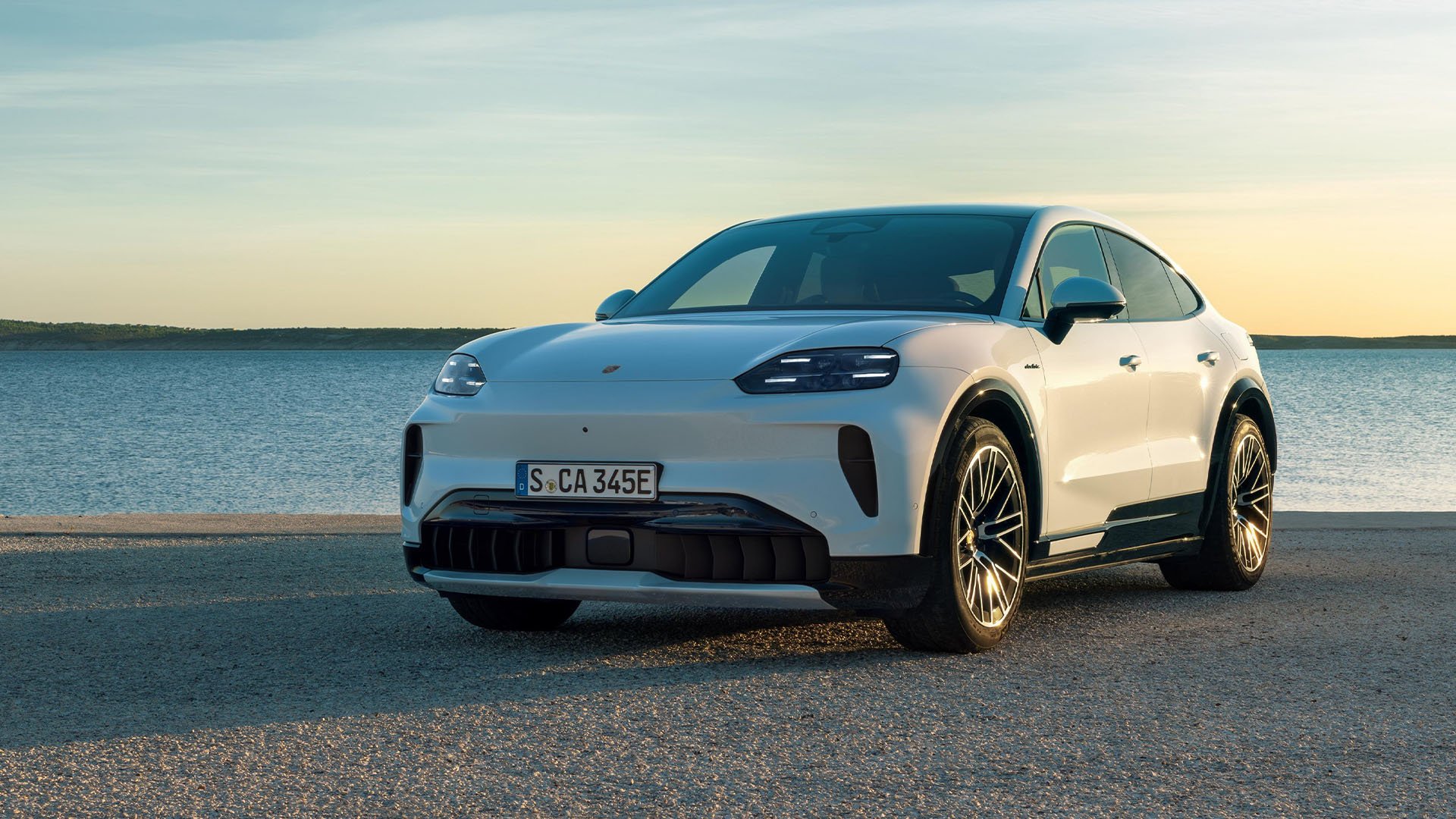 Vit Porsche Cayenne Coupé Electric snett framifrån med havet bakom.