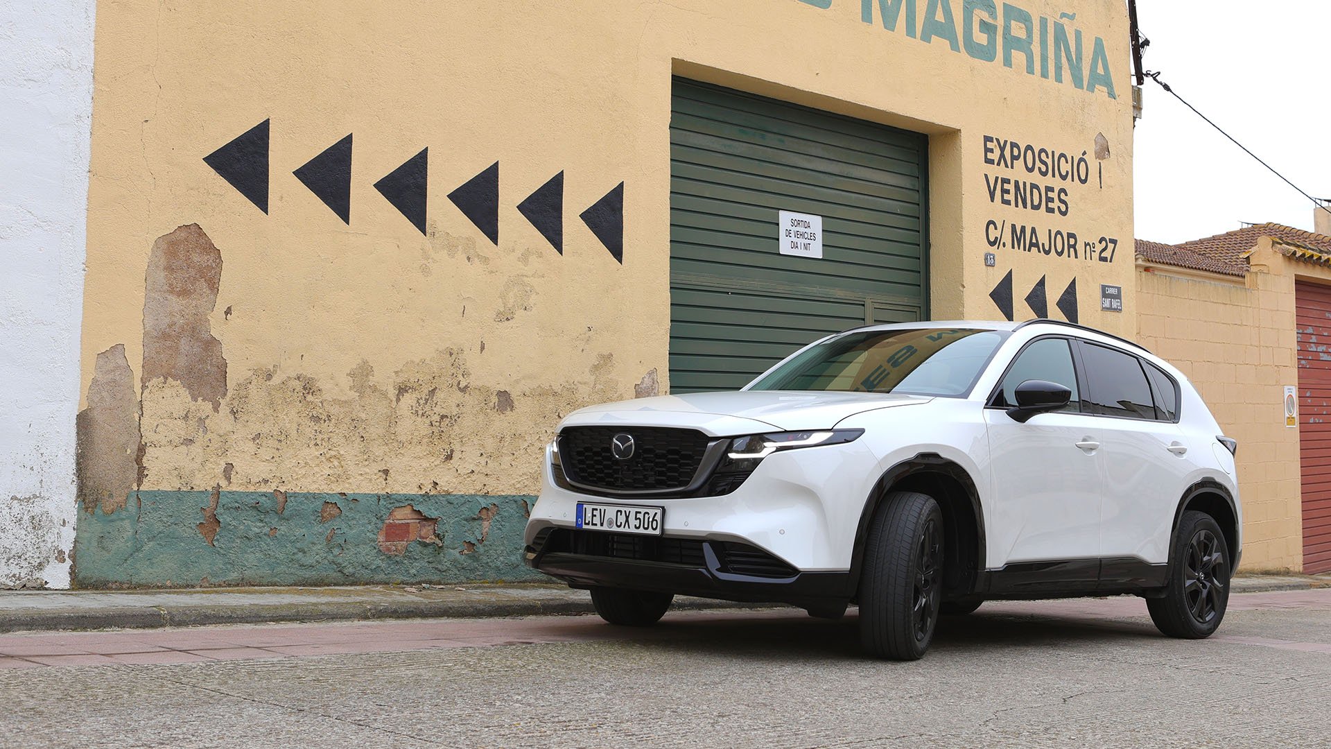 Vit Mazda CX-5 framför en beigefärgad fasad med en grön port.