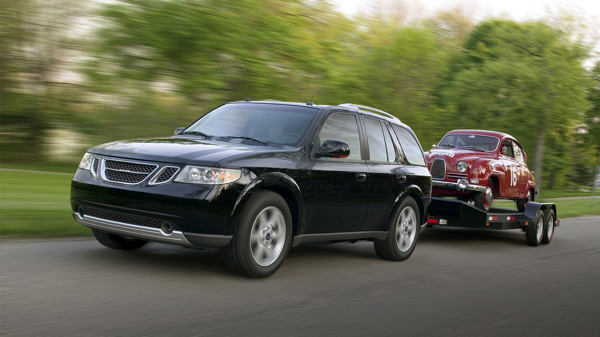 En svart Saab 9-7X drar en släpvagn med en röd Saab 93 på.