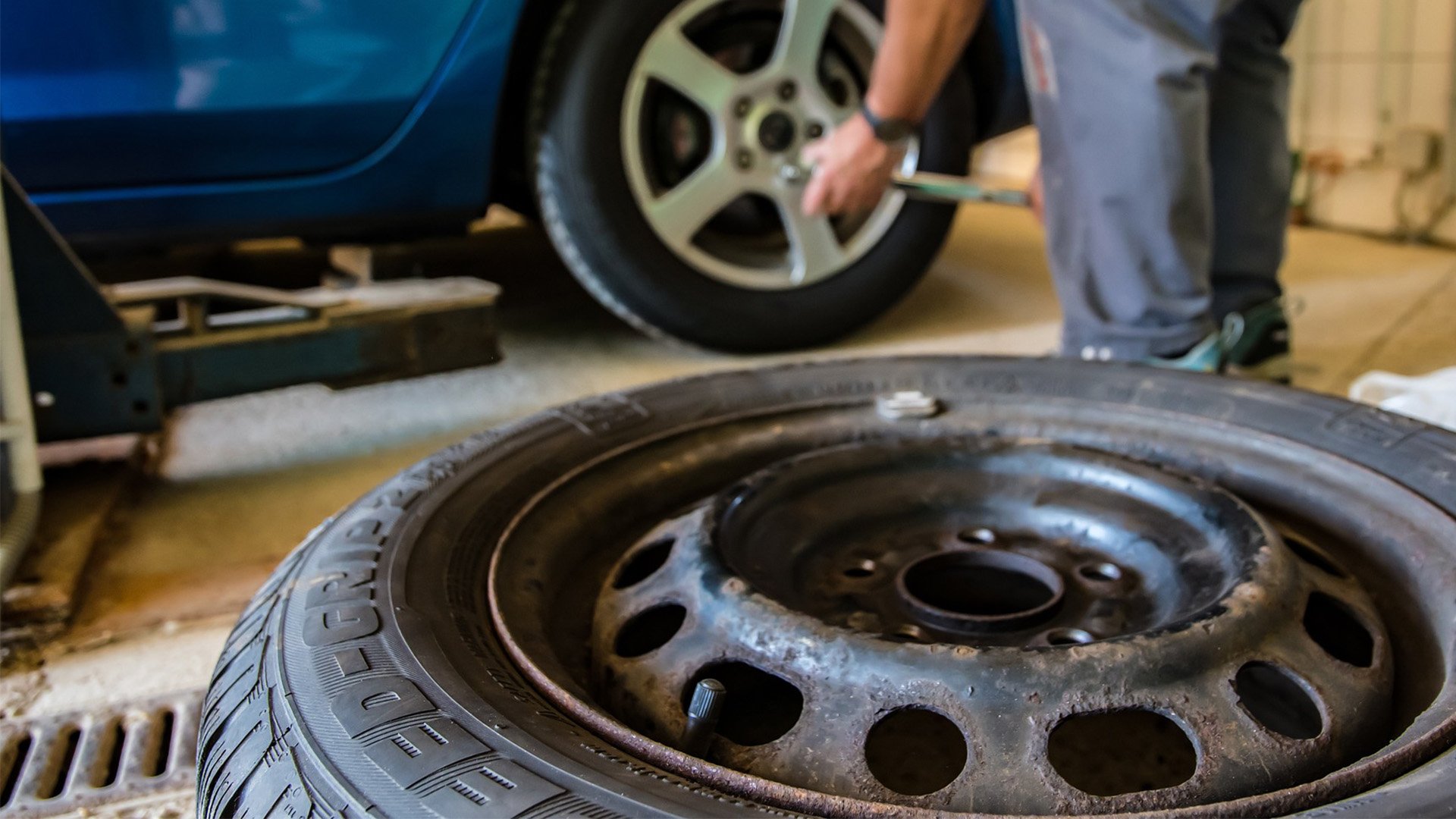 Lossat däck ligger på golvet och en man står i bakgrunden och skruvar på ett nytt däck.