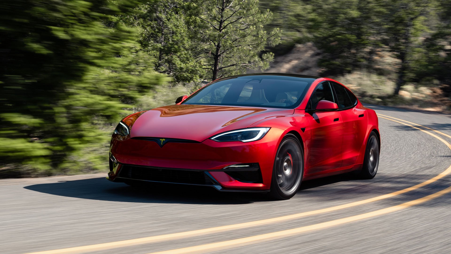 Röd Tesla Model S snett framifrån på landsväg.