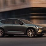 Mörkgrön Volvo EX60 i profil i urban miljö.